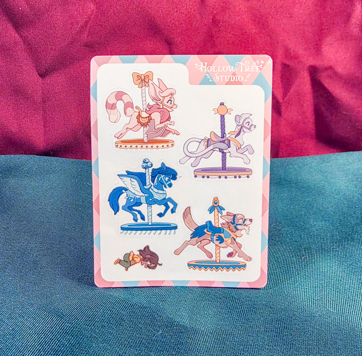 Card with carousel-themed illustrations on a blue and pink fabric background